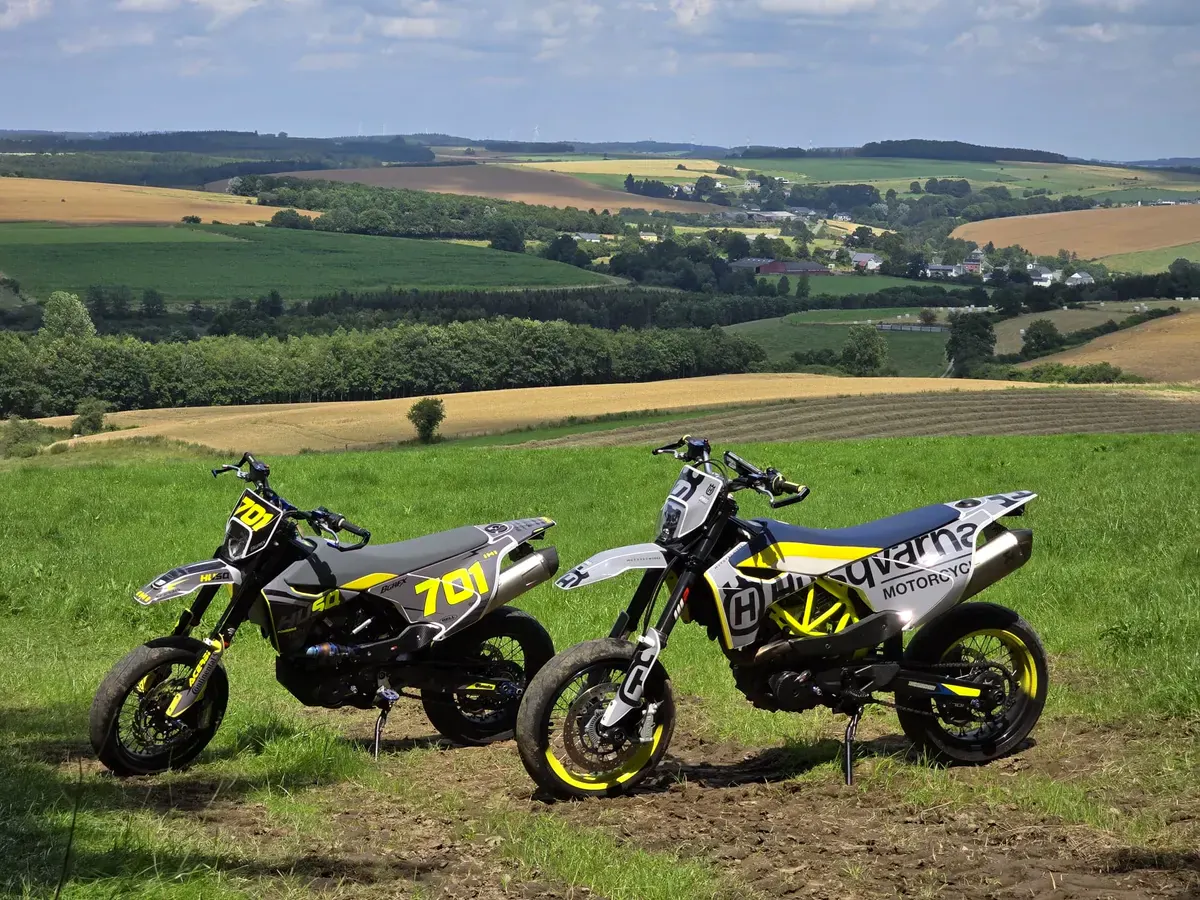 Twee gewrapte Husqvarna 701 supermoto's in een glooiend landschap